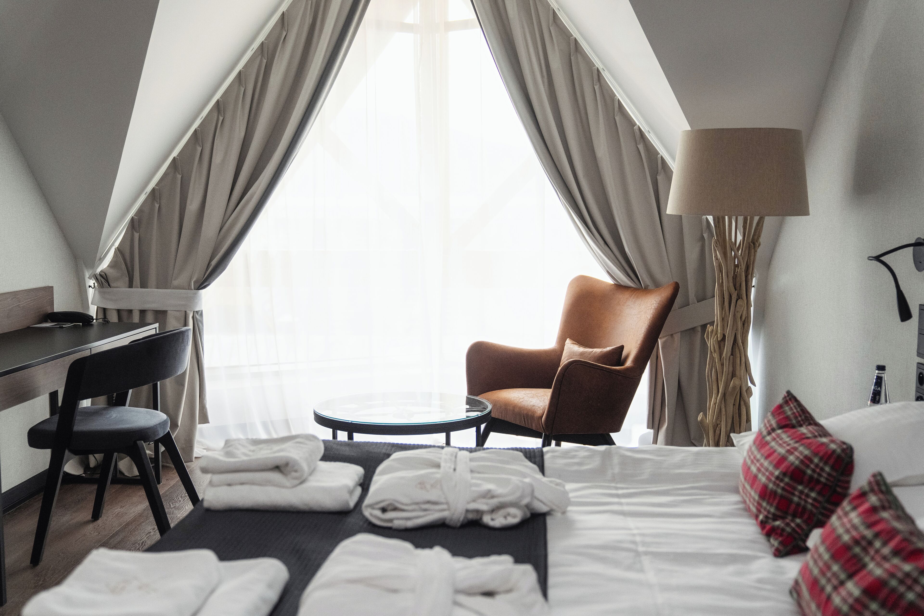 A hotel room with a bed, a chair, a desk, and a lamp.