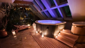 A hot tub surrounded by wooden decking, potted plants, and candles.
