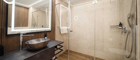 Un baño moderno con un lavabo de piedra, un espejo grande y una zona de ducha con paredes de vidrio.