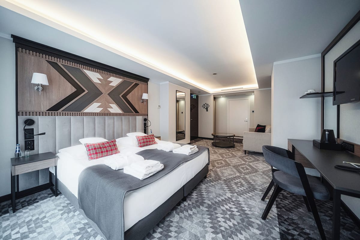 A modern hotel room with a large bed, a desk, a chair, a TV, and a bathroom visible through an open door.