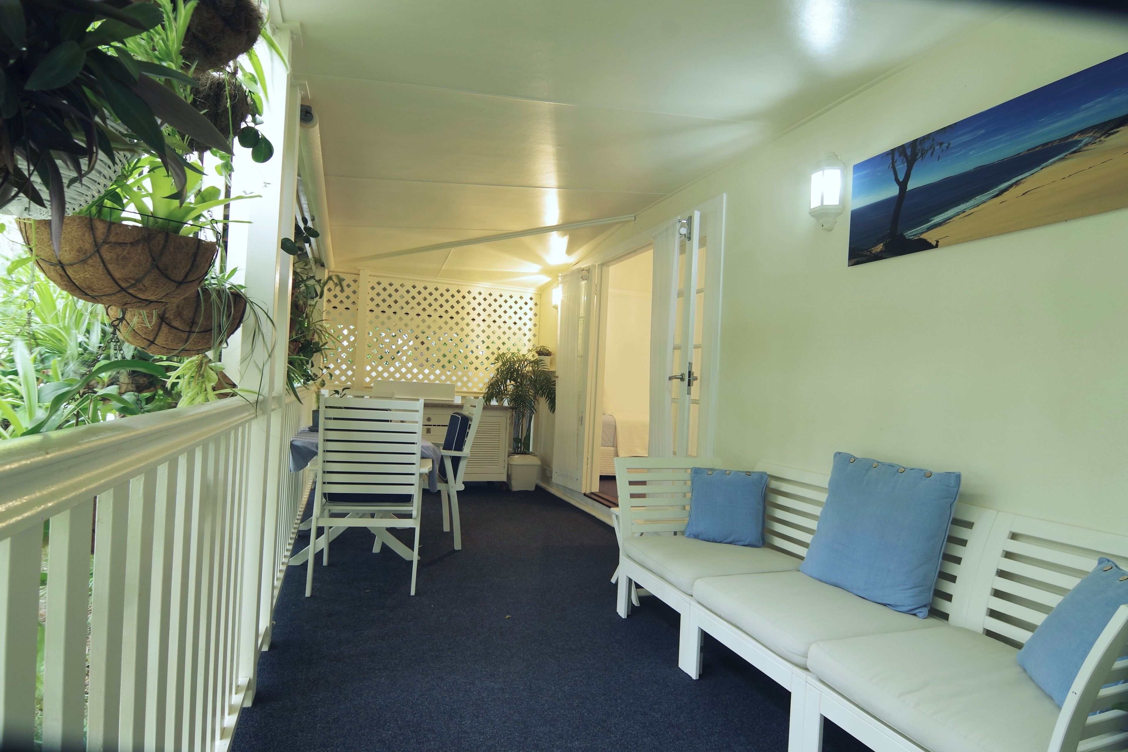 Une véranda avec un banc blanc, une table à manger avec des chaises et des plantes suspendues.