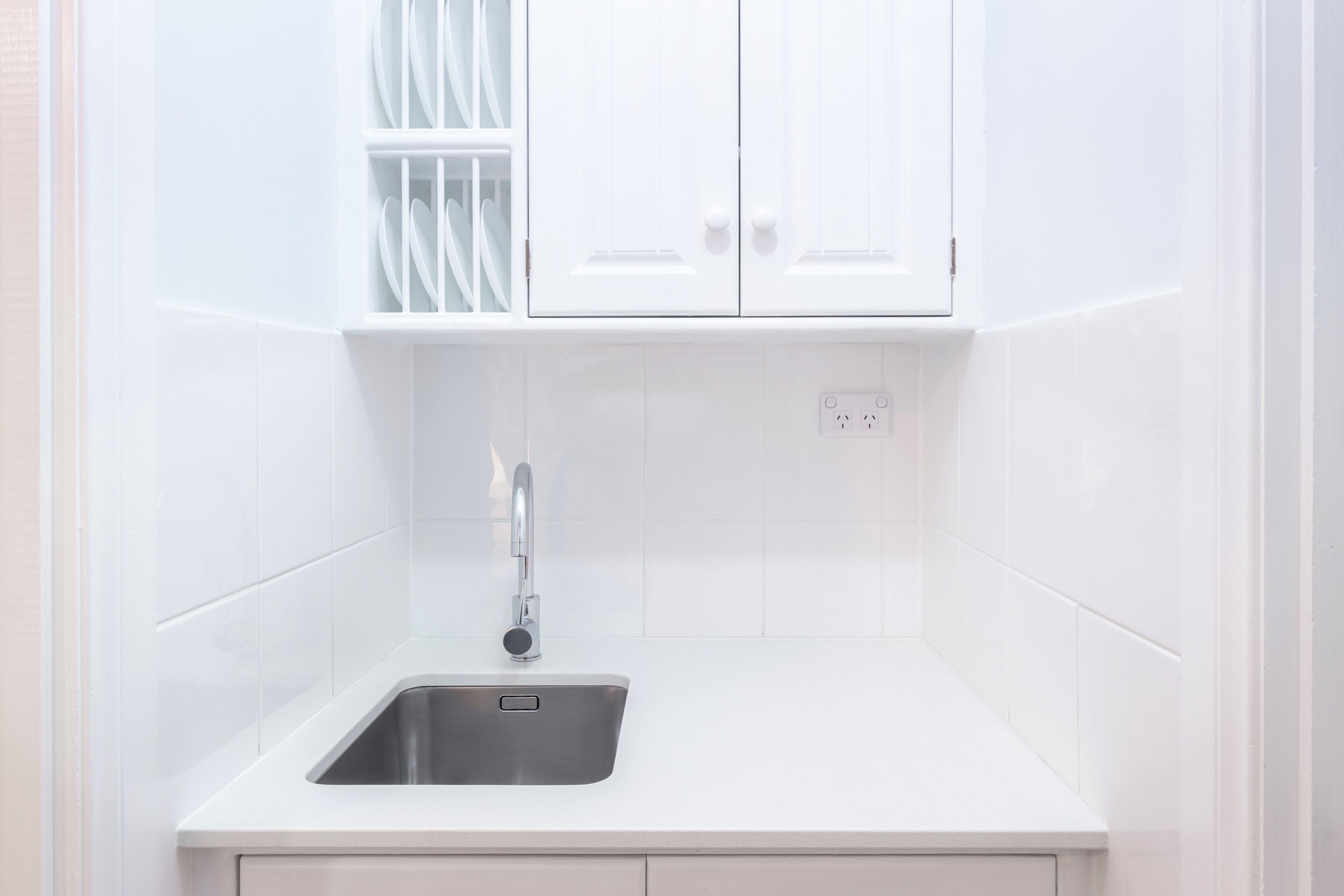A kitchen with white cabinets, a stainless steel sink, and a white countertop.