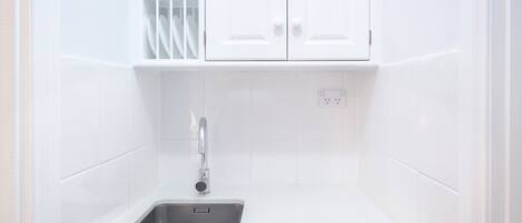 A kitchen with white cabinets, a stainless steel sink, and a white countertop.