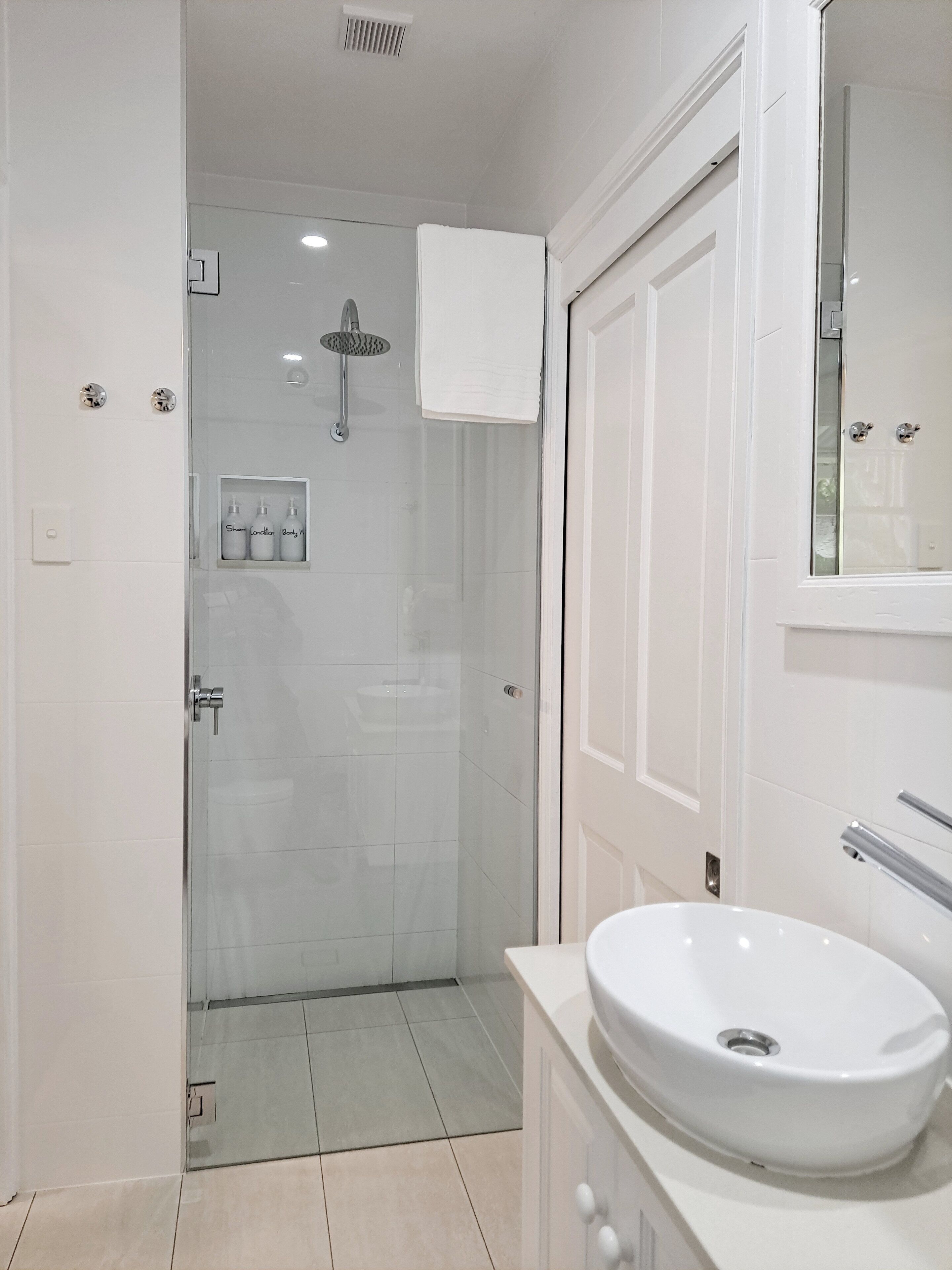 Un baño moderno con ducha envuelta en vidrio, un lavamanos blanco y un espejo sobre él.