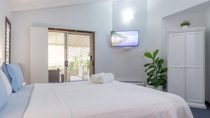 Una habitació d'hotel amb un llit gran, una televisió penjada a la paret, un armari i una planta en test.