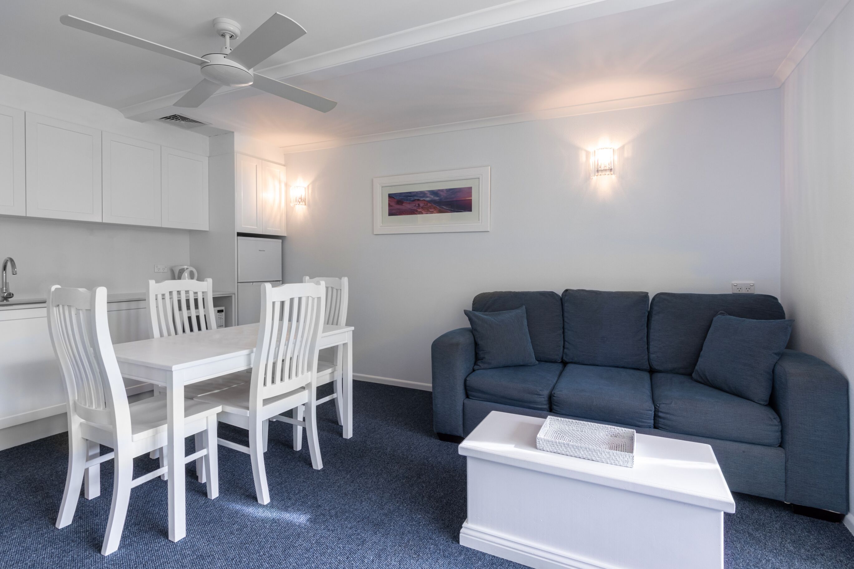 A modern living room with a white dining table, white chairs, a grey sofa, and a white coffee table.