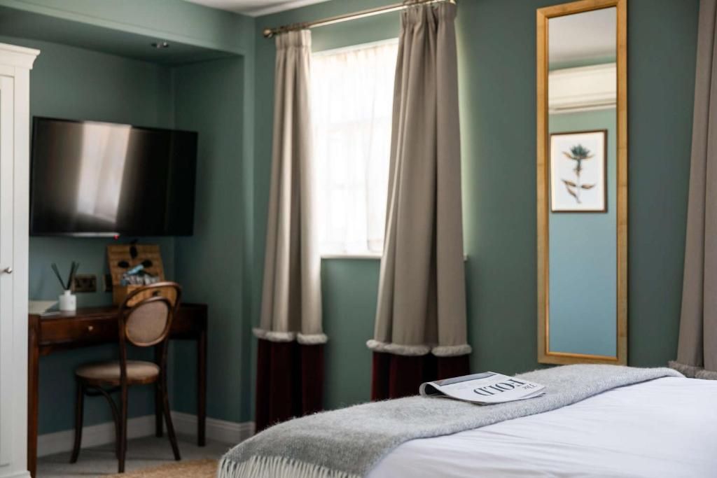 A bedroom with a bed, a desk, a chair, a television, and a window with curtains.