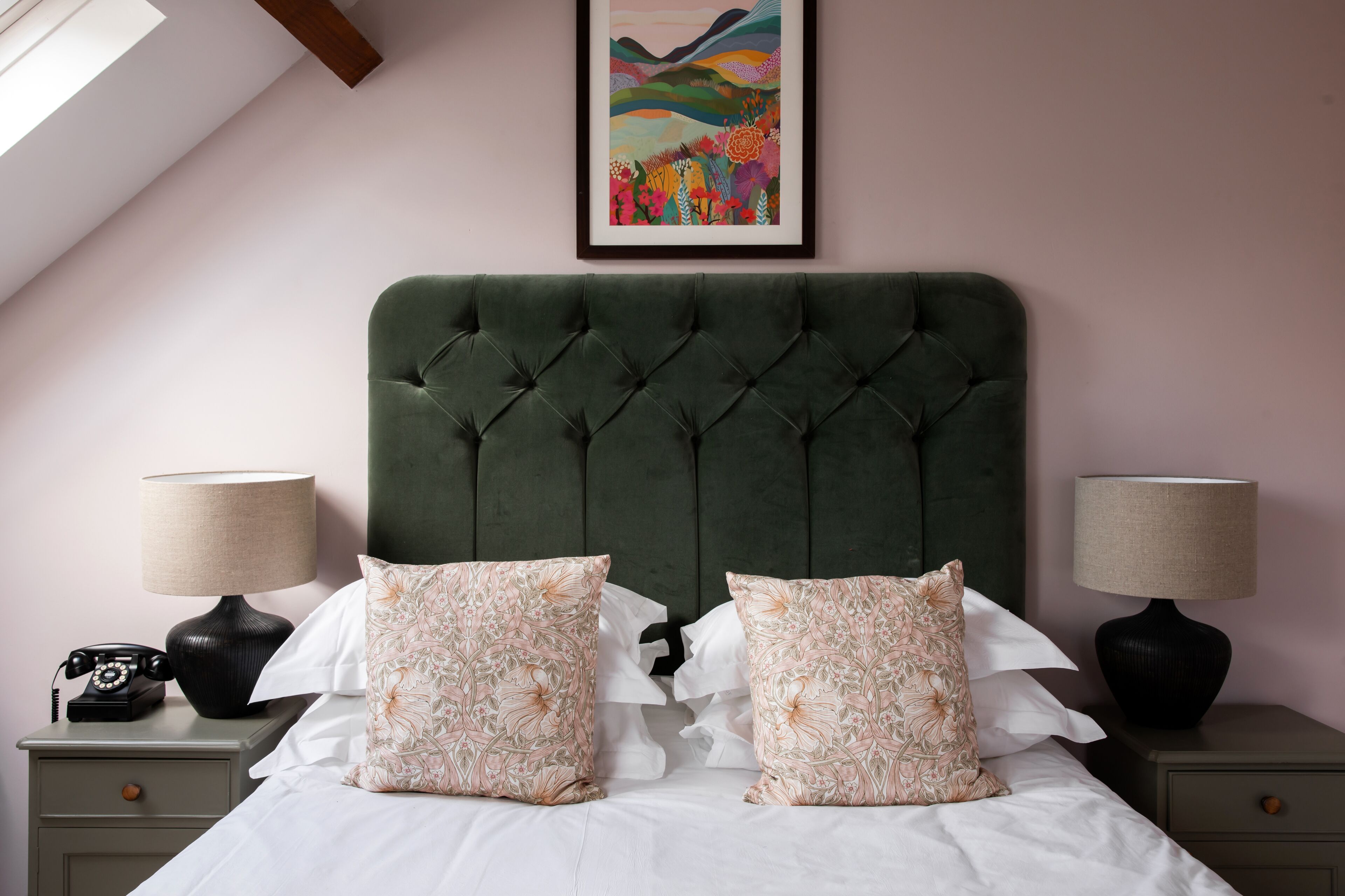 A bedroom with a tufted headboard, floral-patterned pillows, a framed artwork above the bed, and bedside lamps.