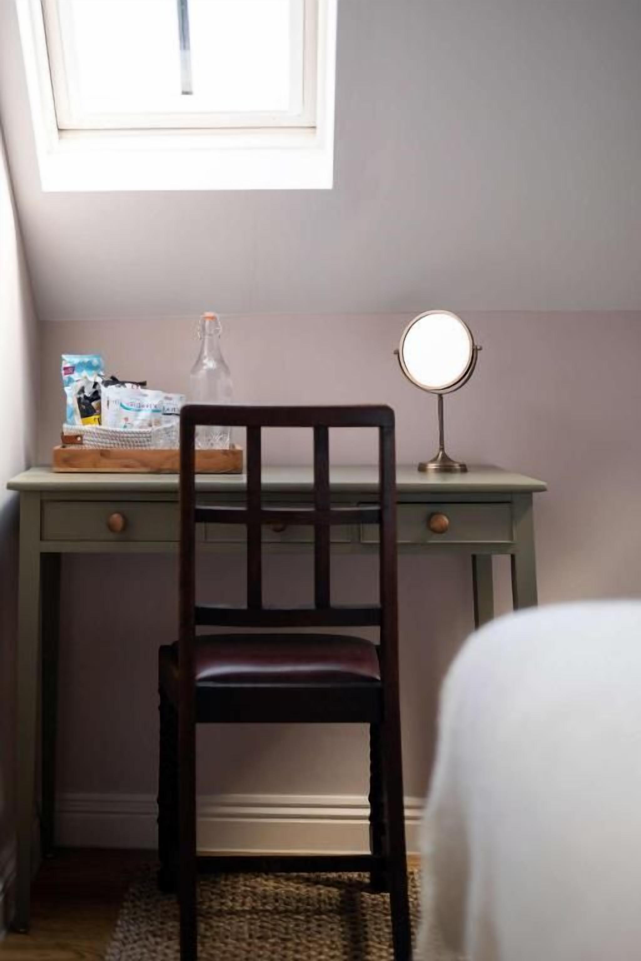 A desk with a chair, a bottle, and a mirror.