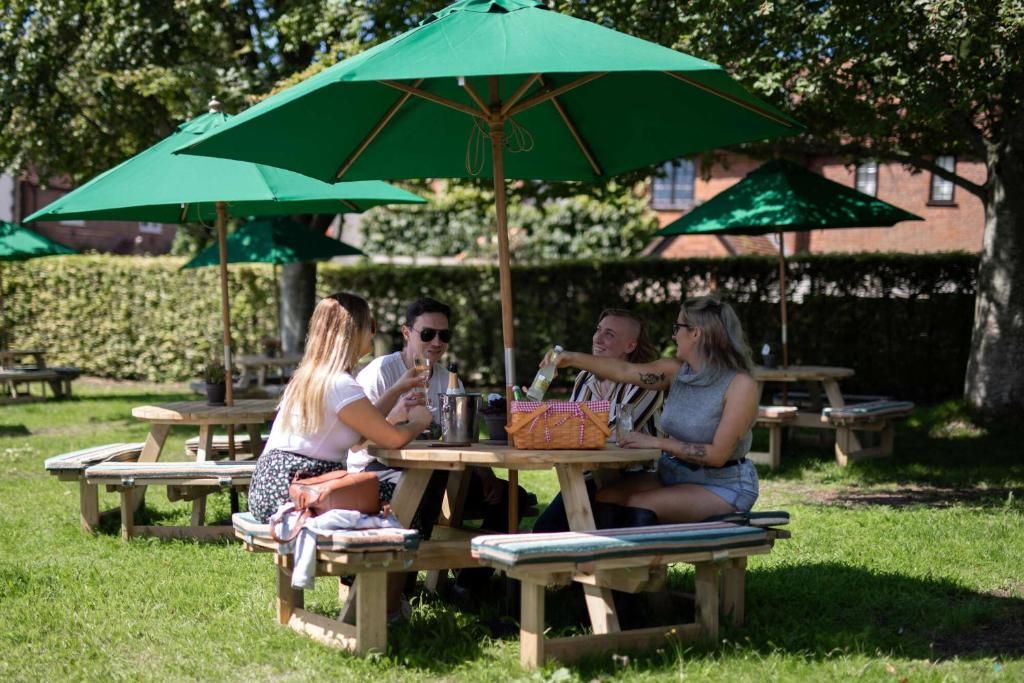 Un área de comedor al aire libre con mesas de picnic de madera y sombrillas verdes.