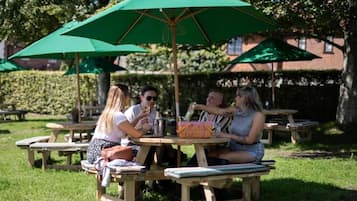 Un área de comedor al aire libre con mesas de picnic de madera y sombrillas verdes.