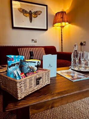 A room with a wooden coffee table, a wicker basket with items, a framed artwork on the wall, a red sofa, and a lamp. - The Lamb Hindon (Salisbury)