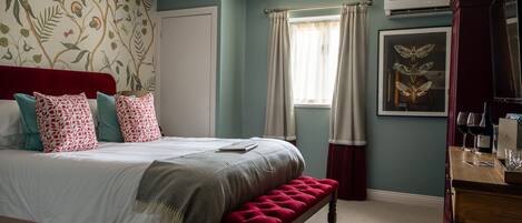 A bedroom with a bed, a bench, a desk, and a framed picture on the wall.