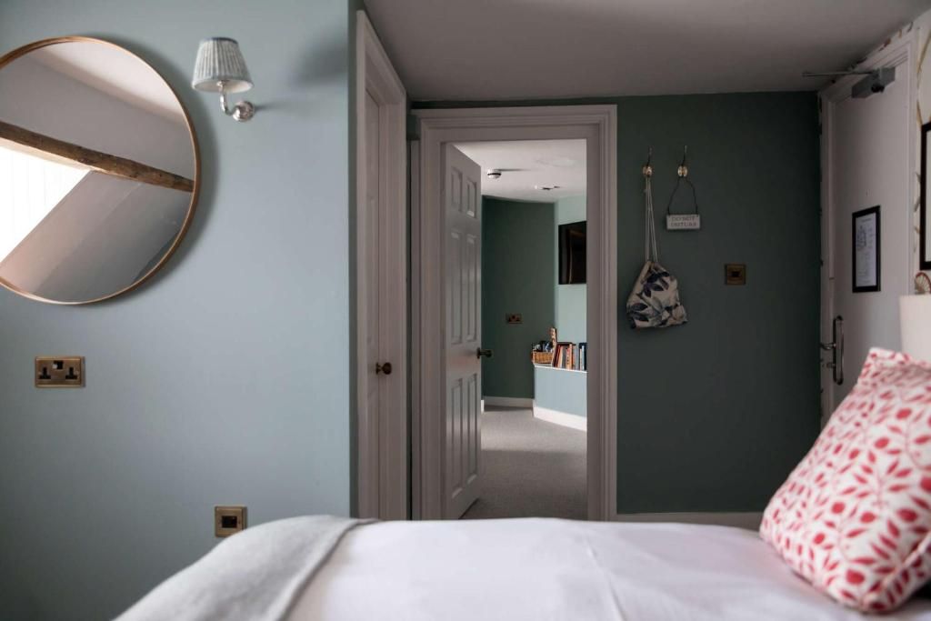 Un dormitorio con cama, un espejo redondo, una lámpara de pared y una puerta que da a otra habitación.