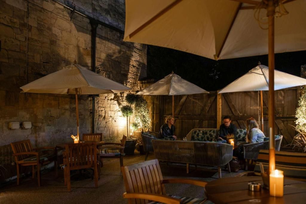 An outdoor seating area with wooden furniture and umbrellas, set against a stone wall.
