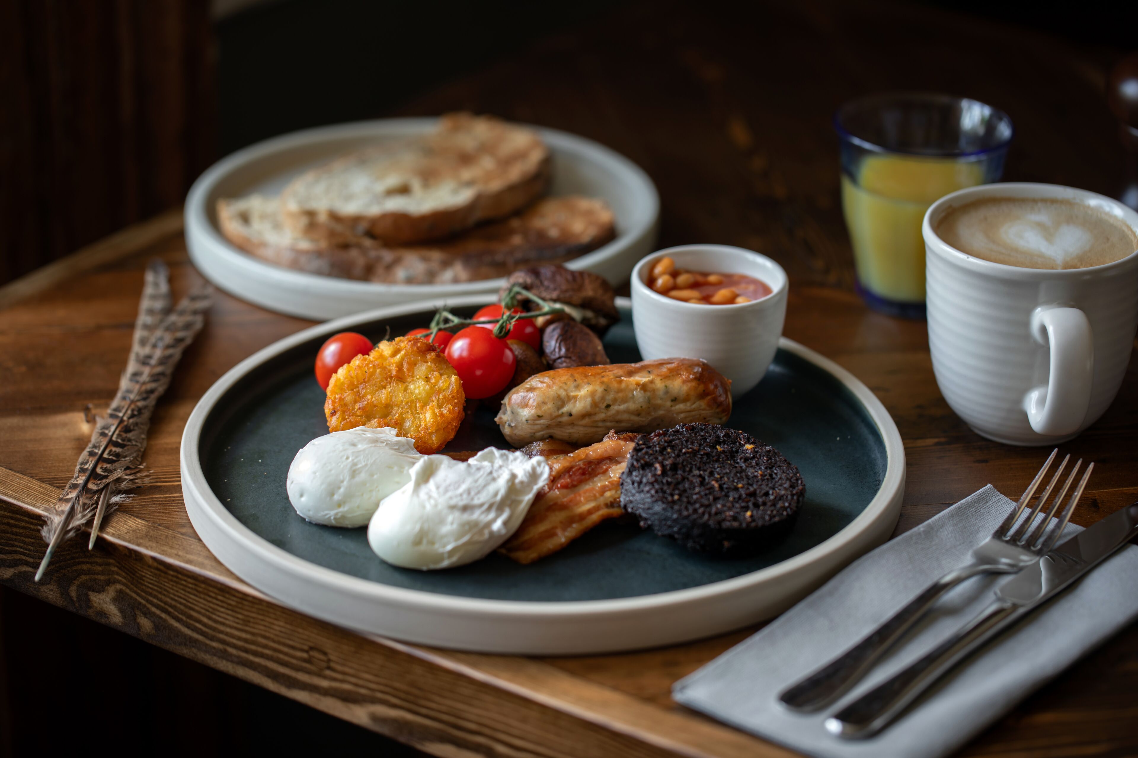 Un plato de desayuno con tostadas, huevos, salchichas, tomates, frijoles y una taza de café.