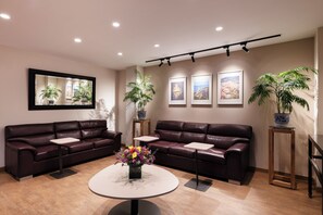 A modern lounge area with leather sofas, a round table with a vase of flowers, and framed artwork on the walls. - San Pablo Hotel (Bogotá)