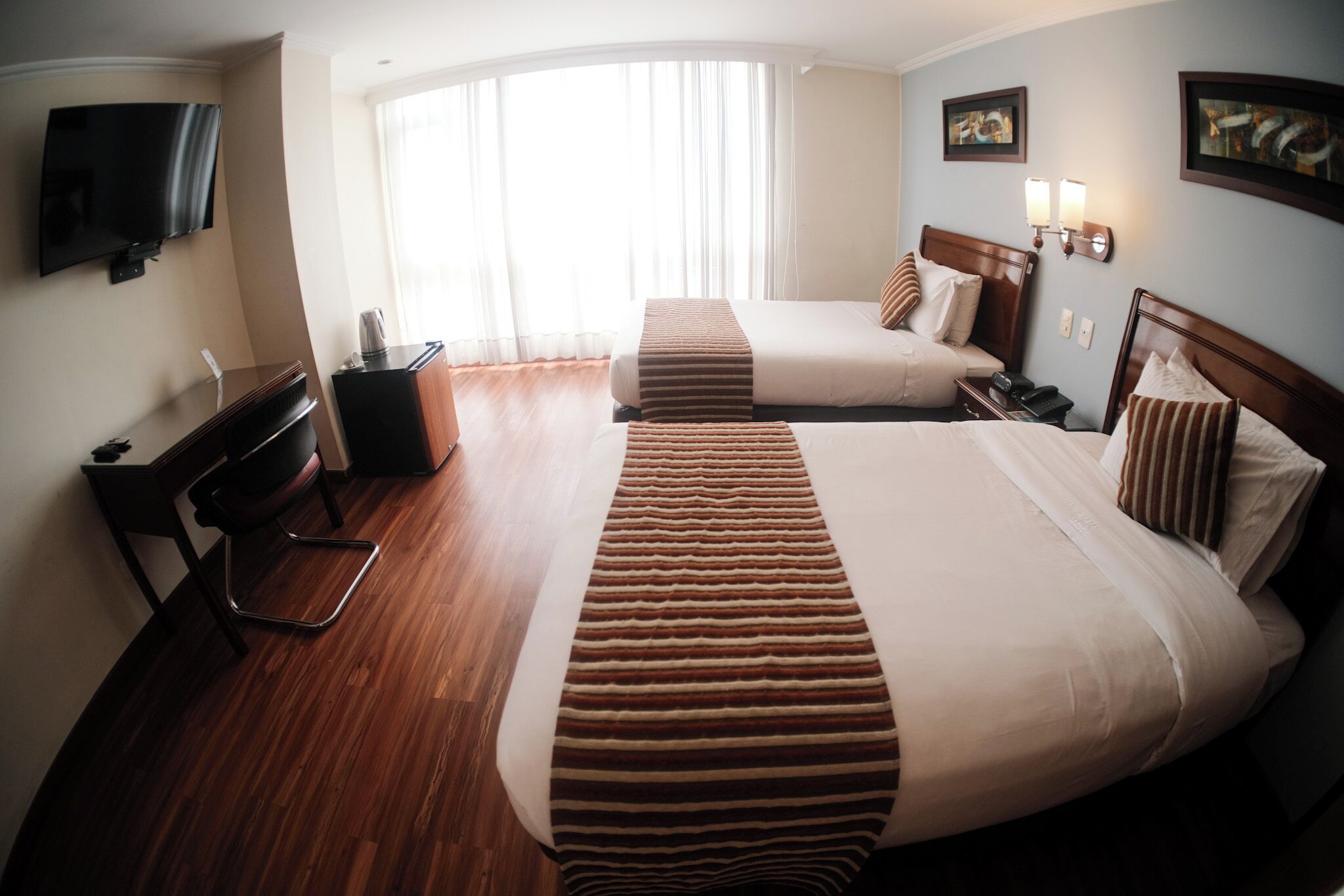 Una habitación de hotel con dos camas, un escritorio, una silla, un televisor y una ventana con cortinas.