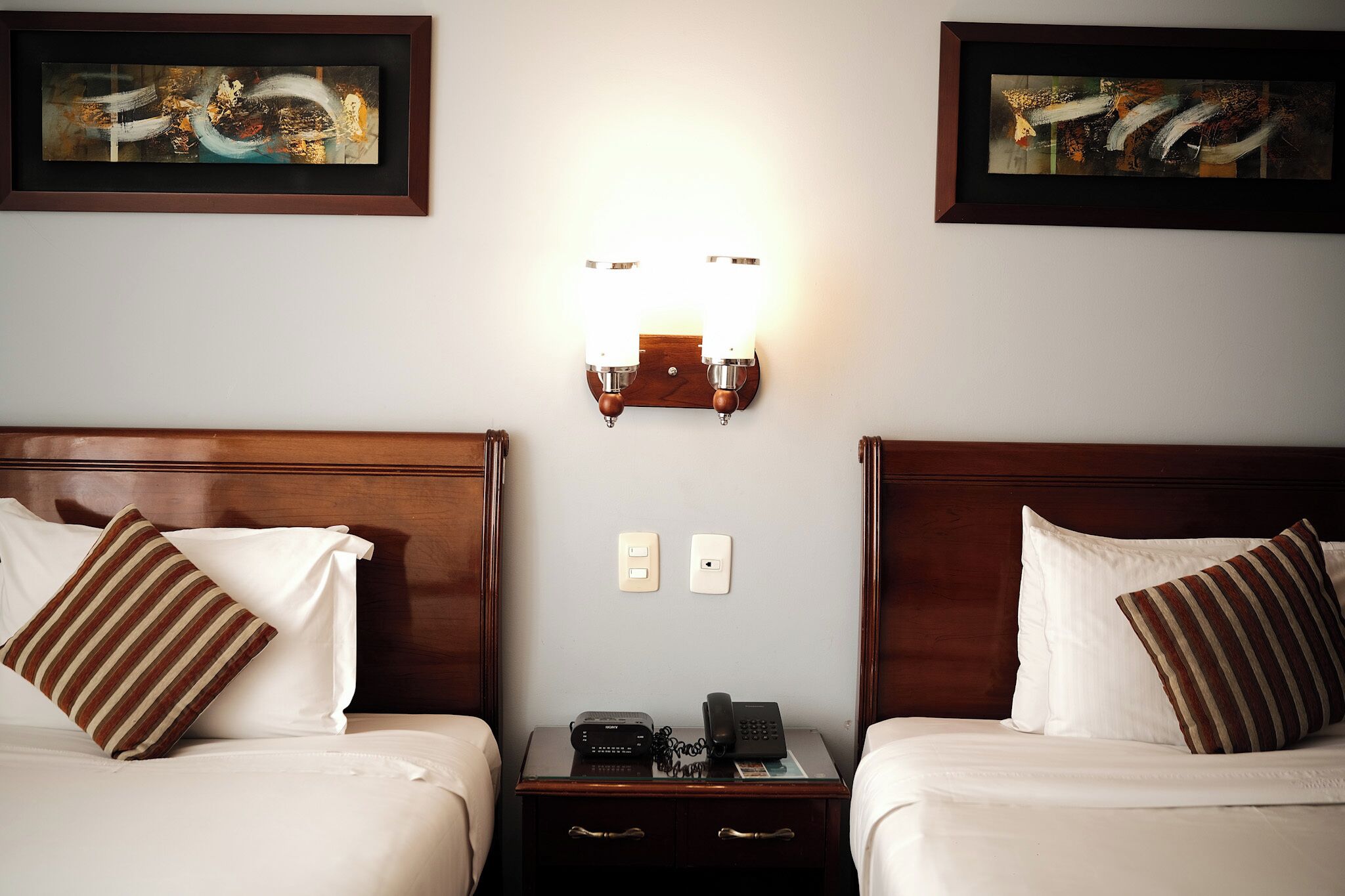 Habitación de hotel con dos camas, una mesita de noche con teléfono y dos obras de arte enmarcadas en las paredes.