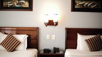 Habitación de hotel con dos camas, una mesita de noche con teléfono y dos obras de arte enmarcadas en las paredes.