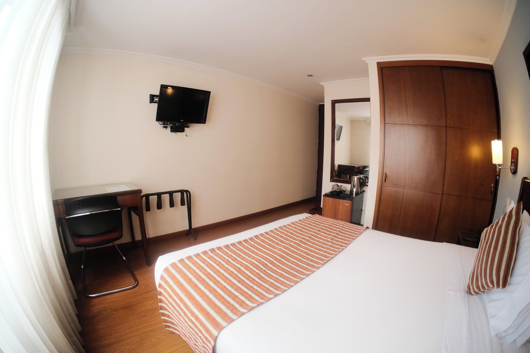 Una habitación de hotel con cama, escritorio, silla, televisor, armario y baño.