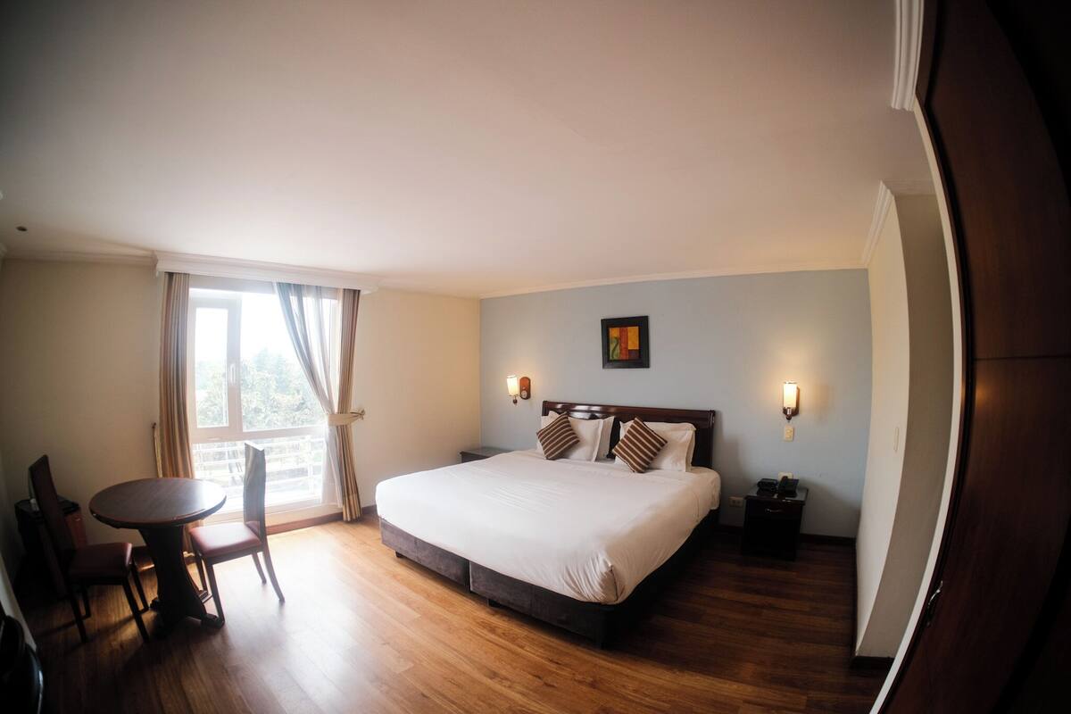 Habitación de hotel con una cama grande, una mesa de comedor y vistas al exterior.