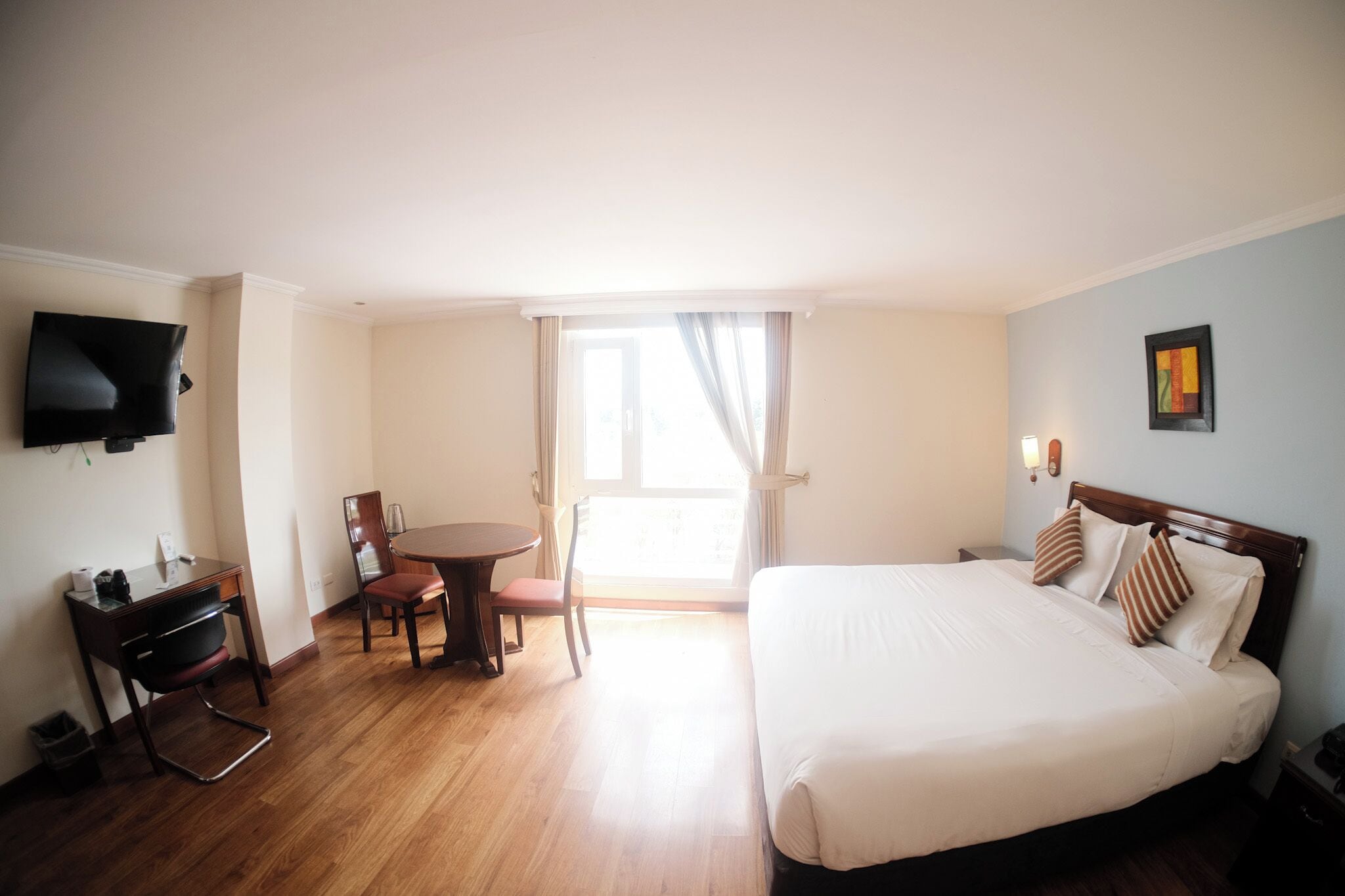 Una habitación de hotel con cama, escritorio, silla, televisión y ventana con cortinas.