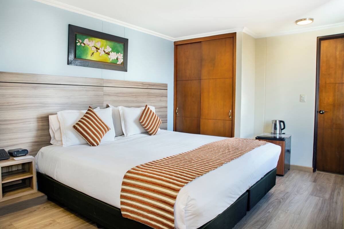 Habitación de hotel con una cama grande, cabecero de madera y un cuadro en la pared.