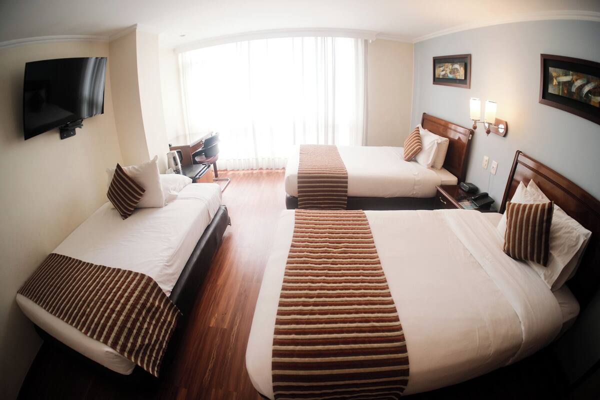 Habitación de hotel con dos camas, un televisor en la pared, un escritorio y una silla.