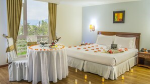 Habitación de hotel con cama, mesita de noche y una mesa redonda con una botella, vasos y una bandeja de fruta.