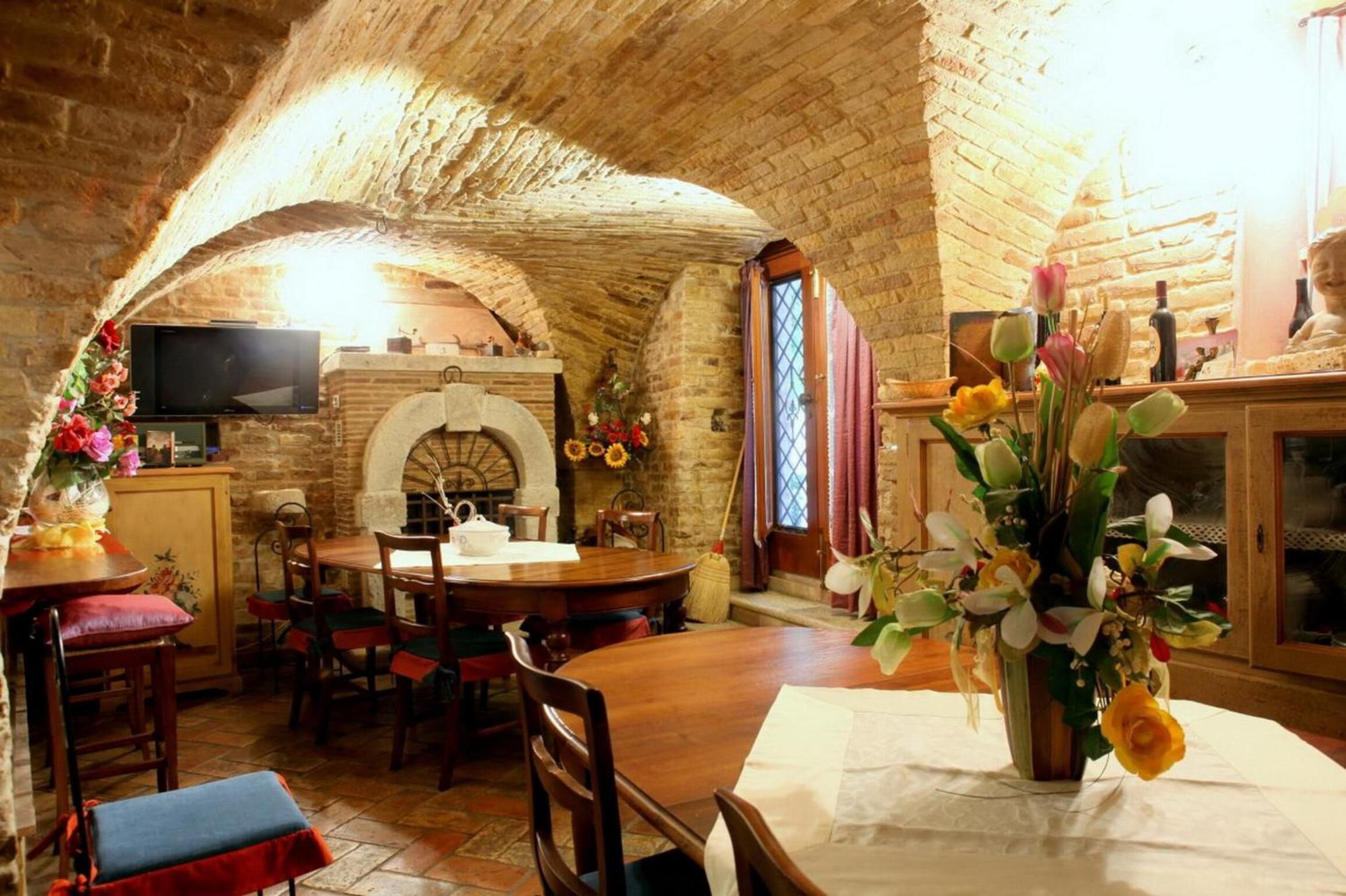 A rustic dining area with a brick ceiling, a fireplace, and a television mounted on the wall.