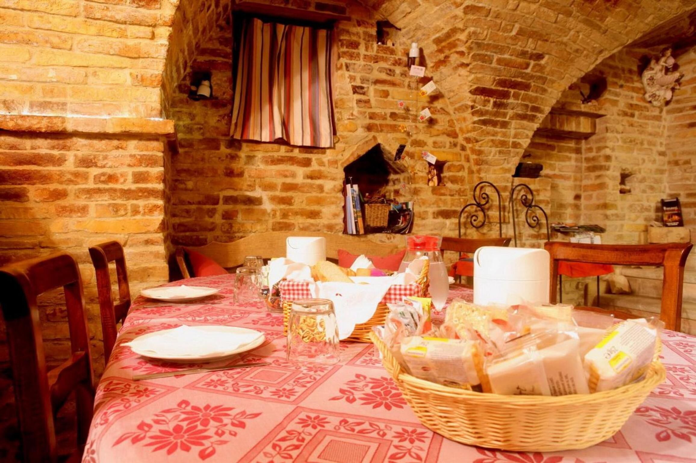 A rustic dining area with a brick wall, a wooden table set with plates, glasses, and a basket of bread.