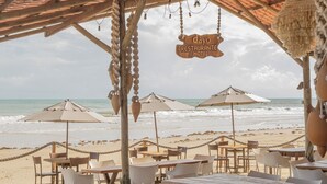 A beachside restaurant with outdoor seating, a wooden pergola, and a view of the ocean. - Dayo Hotel (Trairi)