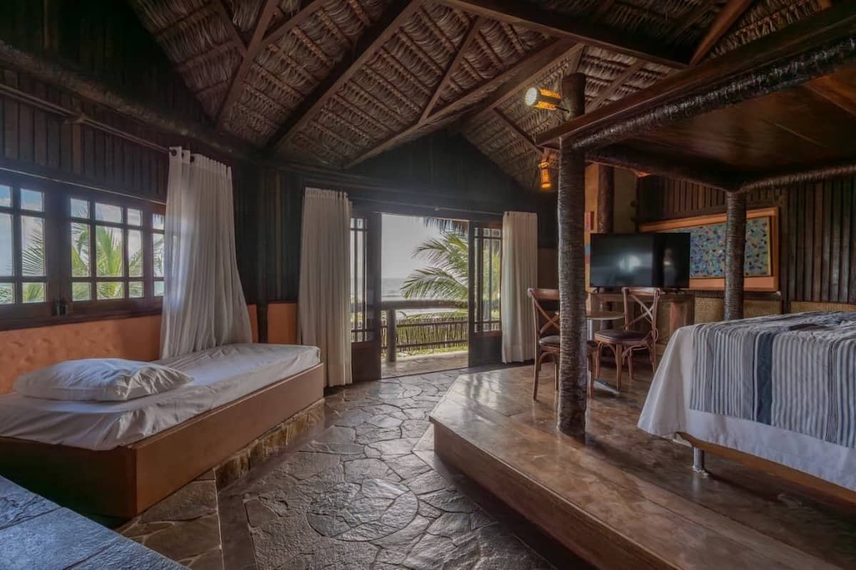 A room with a bed, a television, and a balcony with a view of palm trees.