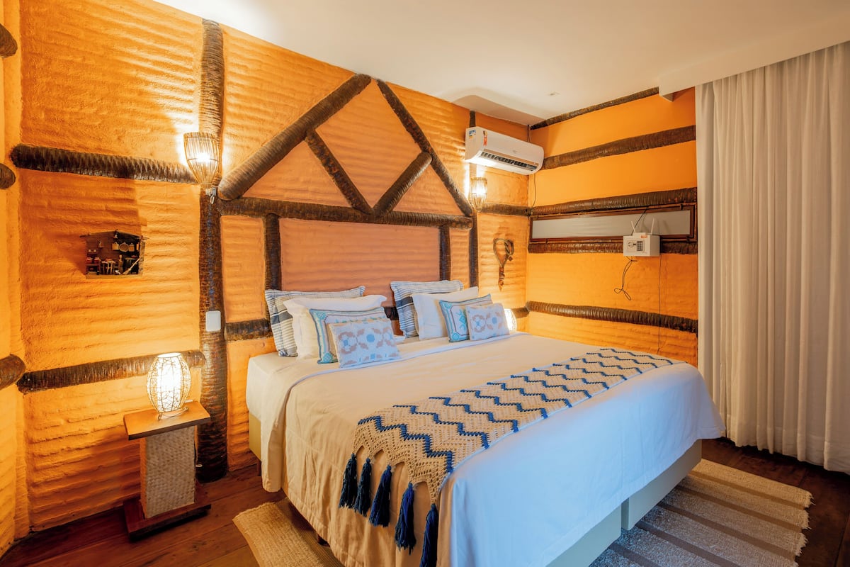 A cozy bedroom with a large bed, a wooden headboard, a bedside lamp, and a wall-mounted air conditioner.