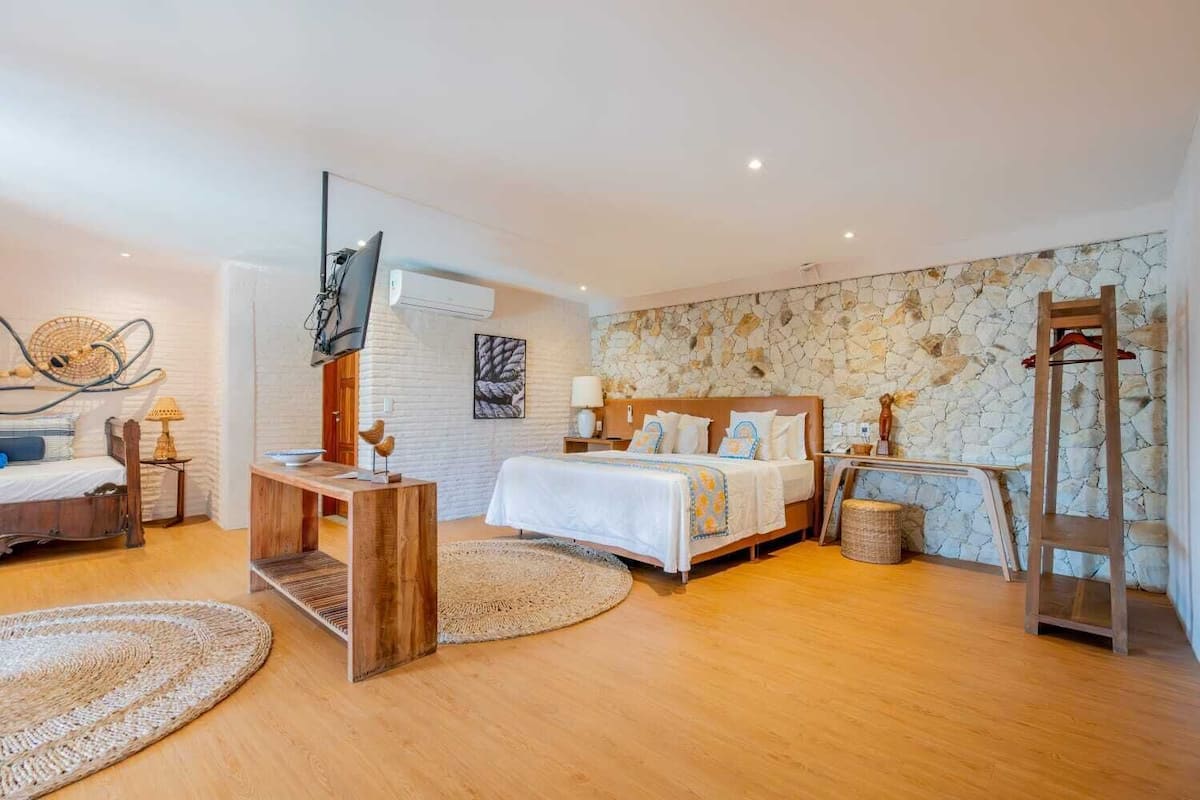 A modern bedroom with a stone wall, a wooden bed, a TV, and a wooden ladder.