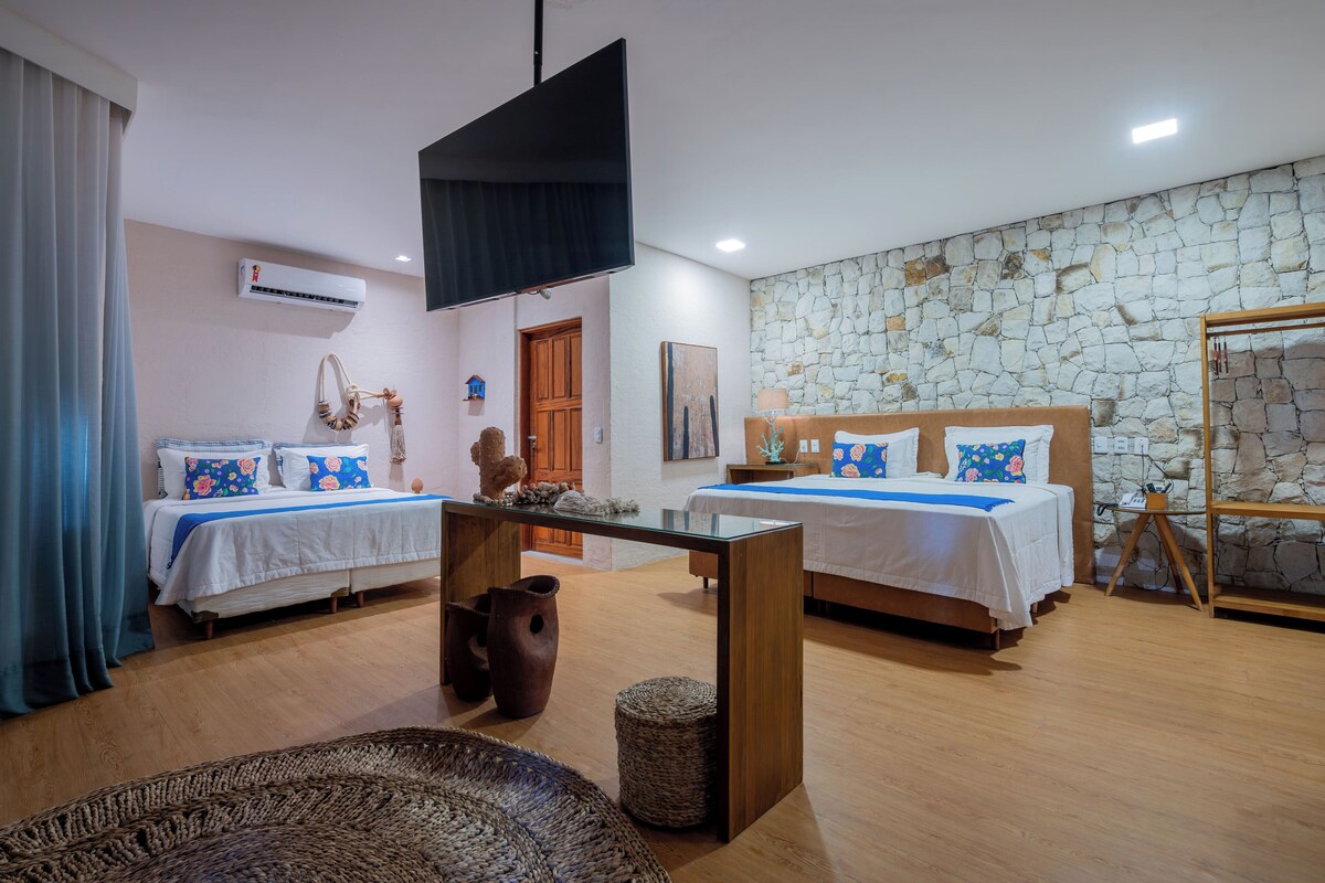A hotel room with two beds, a TV, a stone wall, and a wooden floor.