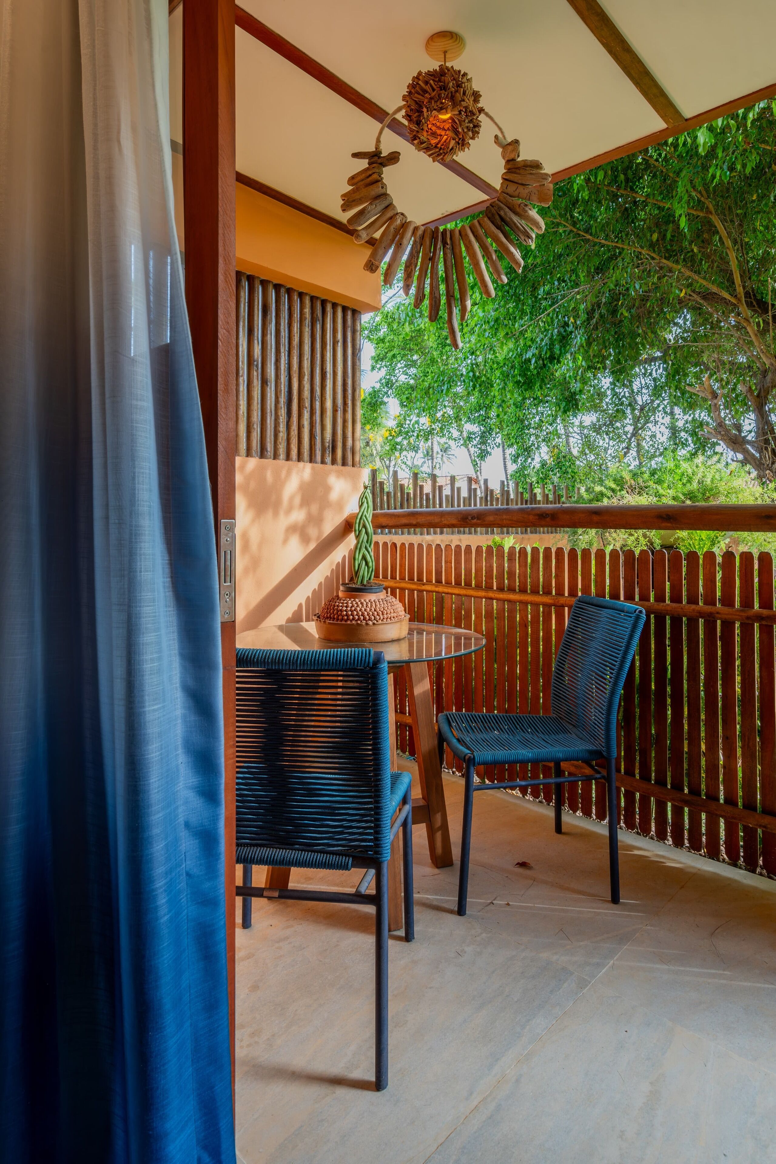 A balcony with a table and two chairs, a wooden fence, and a view of trees.