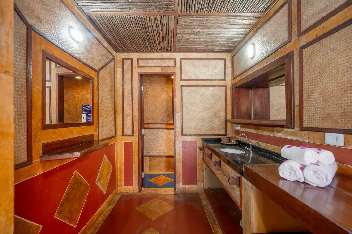 A compact, traditional bathroom with a wooden vanity, a sink, and a mirror. There is a towel rack with towels, and the floor has a patterned design.