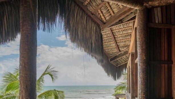 A pool area with a view of the beach, stone walls, and a thatched roof structure. - Dayo Hotel (Trairi)