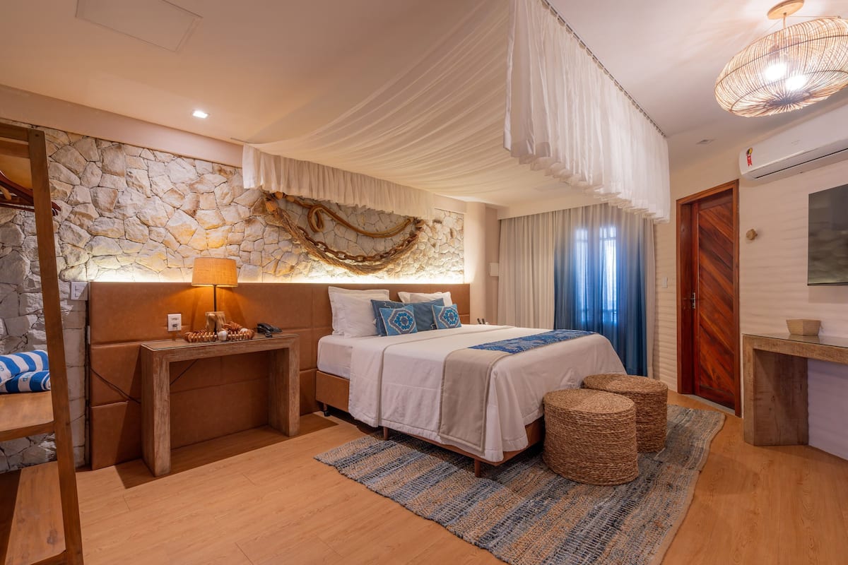 A bedroom with a stone wall, a bed with white bedding, a wooden nightstand, a lamp, and a woven rug.