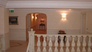A hotel lobby with a white balustrade, a painting on the wall, a small table with flowers, and a staircase leading to another area.