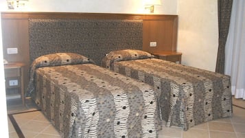 Una habitación de hotel con dos camas, cada una con una colcha de estampado de cebra y almohadas a juego. Hay dos mesitas de noche con lámparas, y el suelo está cubierto de baldosas.