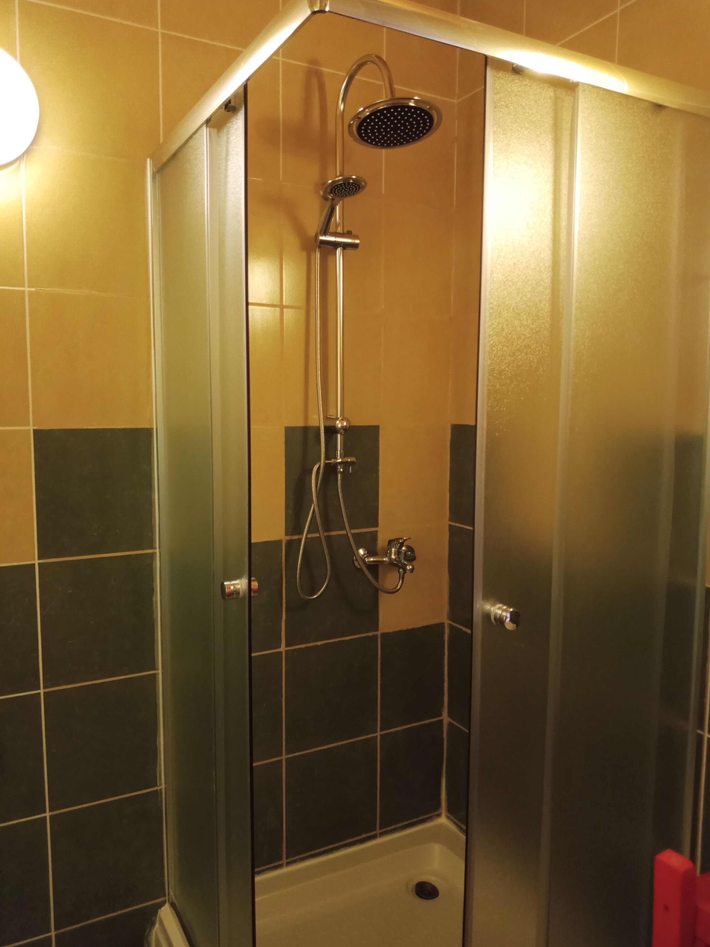 A shower enclosure with a handheld showerhead and a wall-mounted faucet.