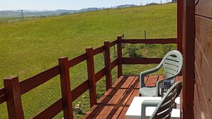 Una terraza de madera con una mesa y sillas, con vista a un campo cubierto de césped y colinas al lejano.