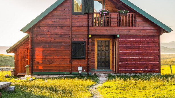 Una cabaña de madera con balcón, puerta principal y un camino que la conduce.