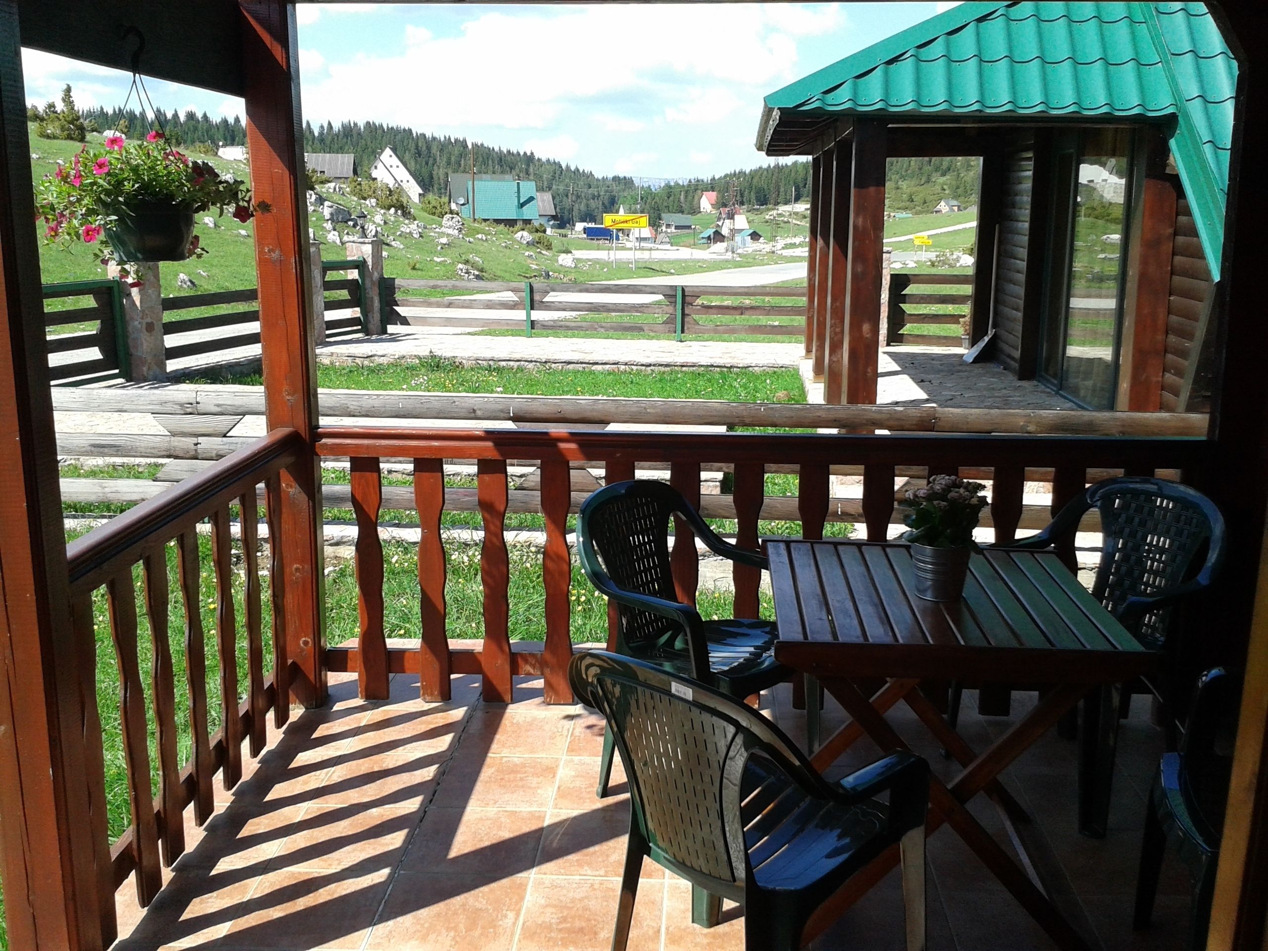 A wooden deck with a table and chairs, overlooking a rural landscape with houses and a green field.