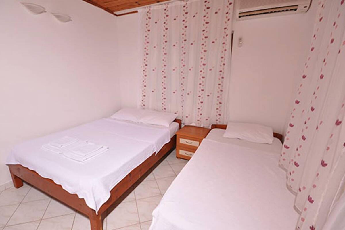 Un dormitorio con dos camas individuales, cabecero de madera, mesita de noche y ventana con cortinas.