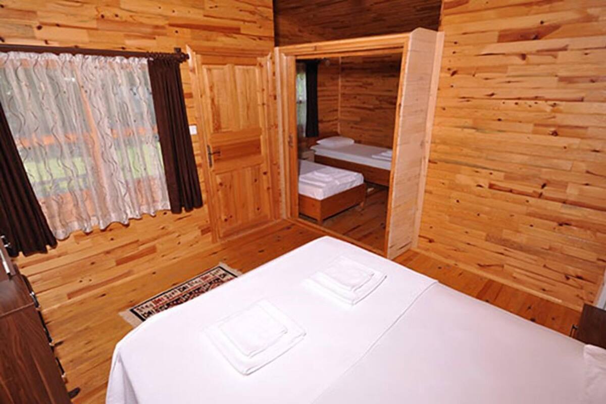 Una habitación de cabaña de madera con una cama, una mesita y una ventana con cortinas.
