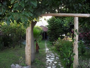 A garden pathway leading to a house with a red roof, surrounded by lush greenery and a wooden pergola. - Cesur Pansiyon (Kemer)
